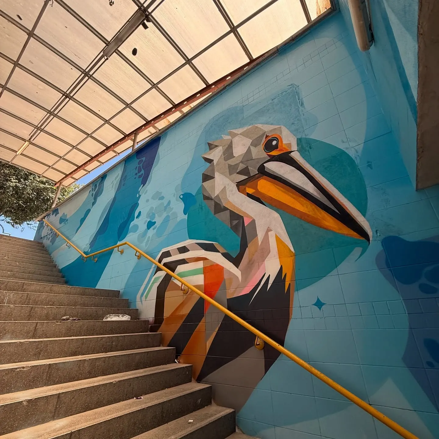 Açık merdiven boyunca uzanan mavi zeminli geometrik kuş muralı